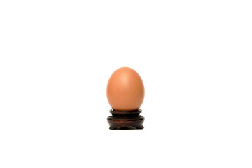 A single brown chicken egg stands upright on a dark, ornate wooden display stand against a pure white background, showcasing its smooth, oval form