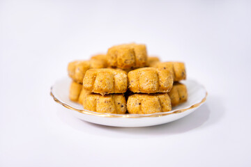 Golden, flower-shaped Taro Biscuit Cookies stacked on a dainty white plate with a gold rim, set against a bright, blurred white background