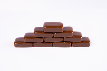 Rich brown coffee candies with a glossy finish are neatly stacked against a pure white background, showcasing a sweet, simple dessert