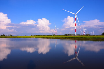 Wind turbines reflected in calm water under blue sky