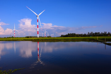 Wind turbines reflected in calm water under blue sky