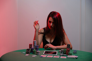 Mysterious girl , red light on her hair, plating poker online concept, tablet in front of her also stack of chips and cards