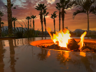 Glowing natural gas fire pit plus ceramic rocks with palm trees and mountains during lovely sunset