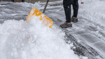 Individual shoveling snow from a driveway with a bright yellow shovel, creating a clear path on a winter day, showcasing winter maintenance efforts