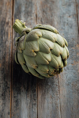 Obraz premium A single fresh artichoke rests on a wooden background. This vegetable showcases its unique shape and color, perfect for culinary inspiration or healthy eating projects.
