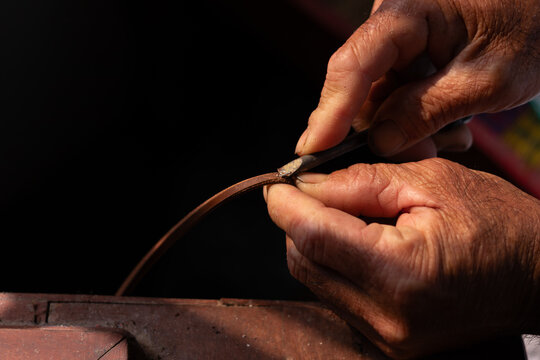 Close up of artisan's hand using a cutting tool to trim a brown leather strip. Handmade craftsmanship and precise leather working process. - Powered by Adobe