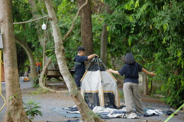 Two People Collaborating to Pitch a Tent at a Forest Campsite