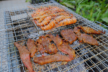 Bright orange prawns and marinated meat slices grilling on a wire grate