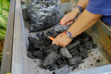 Hand arranging natural wood charcoal in a metal barbecue grill for cooking