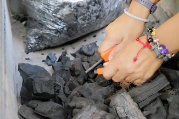 Close-up of hands arranging wood charcoal with an orange tool in a grill