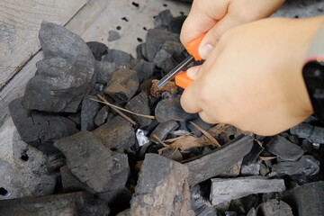 Hands using a fire starter tool to prepare charcoal for grilling
