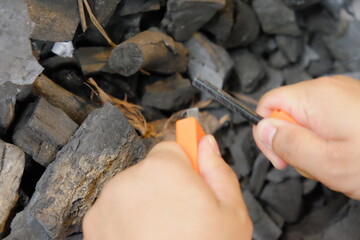 Close-up of hands striking a fire starter over natural wood charcoal