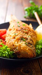 Fried fish on a plate with lettuce, tomato, and lemon, sitting on a wooden surface