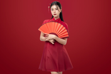 Fototapeta premium Asian woman wearing cheongsam traditional red Chinese dress holding red fan on red background. Symbolizing Chinese New Year, Lunar New Year celebration, good fortune and happiness.