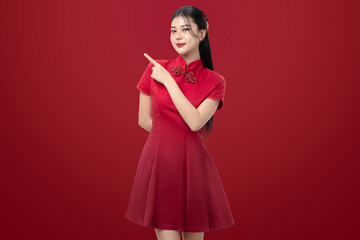 Asian woman in a traditional red Chinese dress pointing finger to the side. Studio portrait on a red background with copy space, representing Chinese New Year, Lunar New Year, promotion and festive.