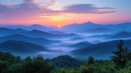 Fototapeta premium Sunrise over mist-covered layered mountain ranges with vibrant sky colors and lush green forest in foreground