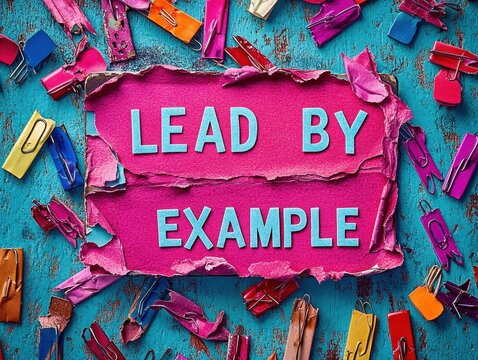 Colorful torn paper revealing the phrase lead by example surrounded by vibrant torn paper clips on a rustic blue wooden surface conveying motivation and leadership