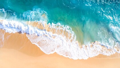 Aerial view of a sandy beach as turquoise ocean waves crash ashore. The foam creates a textured pattern contrasting with the smooth sand