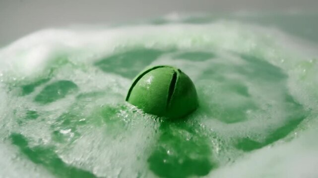 Woman drops green bath bomb into water causing a fizzy reaction
