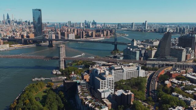 Wide panoramic aerial view of the Brooklyn and Manhattan Bridges crossing the East River, set against the towering skylines of Manhattan and Brooklyn