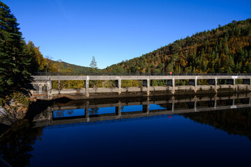 Fototapeta premium Cruacha dam and walkway in fall Scottish woodland with golden birch trees, hydroelectric dam electric power generation Loch Beinn o Mheadhain, Glen Affric, Scotland, UK 