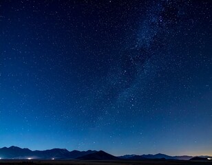 Deep blue night sky dotted with numerous shining stars over silhouette mountains