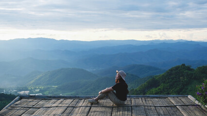 Obraz premium A woman sitting on wooden terrace and looking at a mountain view before sunset