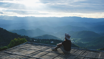 A woman sitting on wooden terrace and looking at a mountain view before sunset