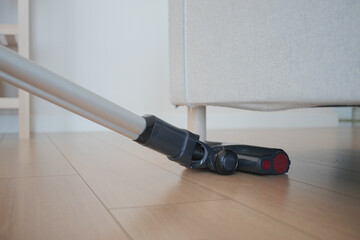 Vacuum cleaner in action on wooden floor near sofa