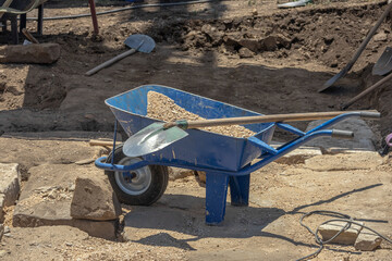 A single-wheeled metal trolley for transporting various materials on a construction site. Construction equipment. Manual labor during restoration work. A shovel on a cart.