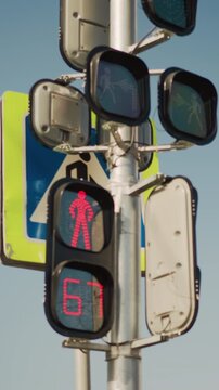 red pedestrian signal countdown on pole, urban intersection closeup showing LED timer decreasing from to , red walking silhouette illuminated, signage and metal housing visible against clear