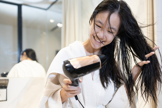 Young girl drying her hair with blow dryer after washing,daily beauty and hygiene routine,hair care,scalp care,freshness,self care lifestyle at home,Smiling asian woman blow drying hair after shower