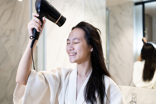 Young girl drying her hair with a blow dryer after washing,daily beauty and hygiene routine,hair care,scalp care,freshness,lifestyle at home,Smiling woman blow drying hair after shower in bathroom