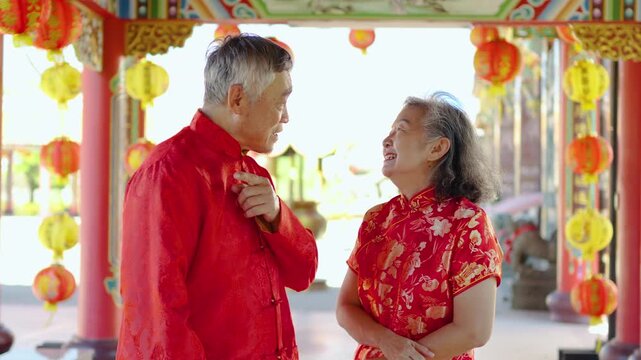 An elderly asian couple in bright cheongsams visits a colorful temple to pray, sharing laughter and stories while embracing the warmth of the Chinese New Year celebration with joy and love.