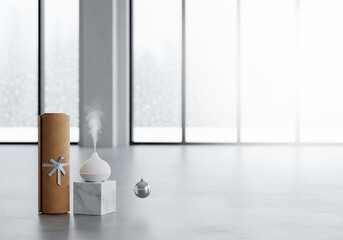 A modern wellness setup featuring an essential oil diffuser releasing steam, a yoga mat roll, and a silver Christmas ornament on a polished marble block in a bright, open space.