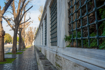 Historic mosque wall with decorative iron lattice windows and stone pathway lined with bare trees in Sultanahmet Square Istanbul Turkey Ottoman architecture detail
