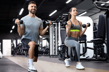Attractive sports people are working out with dumbbells at gym.