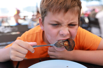 Excited boy eating mushroom with fork at outdoor restaurant