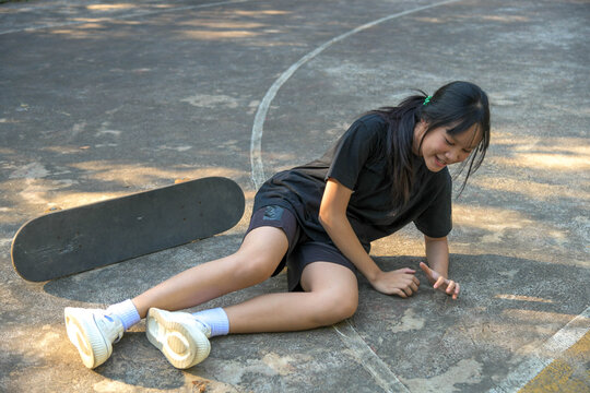 A young skateboarder sitting on the ground after falling, smiling through the moment.
