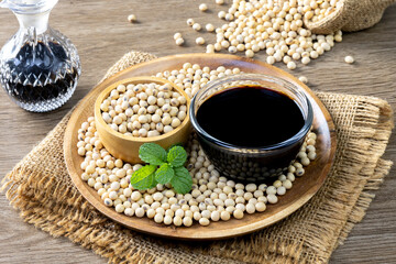 Soy sauce in a glass bowl and soybeans on a wooden plate.