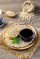Soy sauce in a glass bowl and soybeans on a wooden plate.