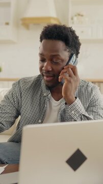 Multitasking male freelancer talking by phone and working with laptop at home workplace. Vertical portrait of businessman or office worker in distance mode, online job for web-developer or designer