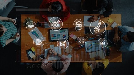A diverse group of professionals collaborates in an office setting, engaging in strategic planning while surrounded by colorful charts and digital graphics on the table. Raster