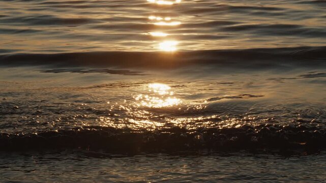 Lake with gentle calm waves rolling over the sandy beach during sunset