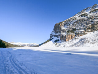 Winter Rocky Mountains - Frozen Lake Louise covered in snow, snow-capped mountains and forest, ...