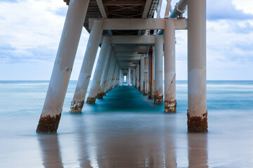 Looking out beneath the iconic Sand Pumping Jetty at The Spit, the Gold Coast's northernmost beach in Queensland. Captured using a long exposure on an overcast cloudy morning.