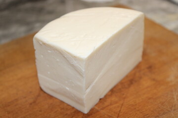Block of cheese sits on a wooden cutting board in a kitchen setting during the daytime
