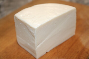 Block of fresh white cheese on wooden cutting board in kitchen setting suitable for various dishes and recipes