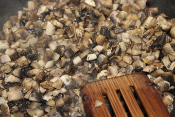 Chopped mushrooms cooking in a pan with wooden spatula at home kitchen during meal preparation time
