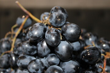 Fresh black grapes are piled together in a close view showing their shiny skin and water droplets in a market setting